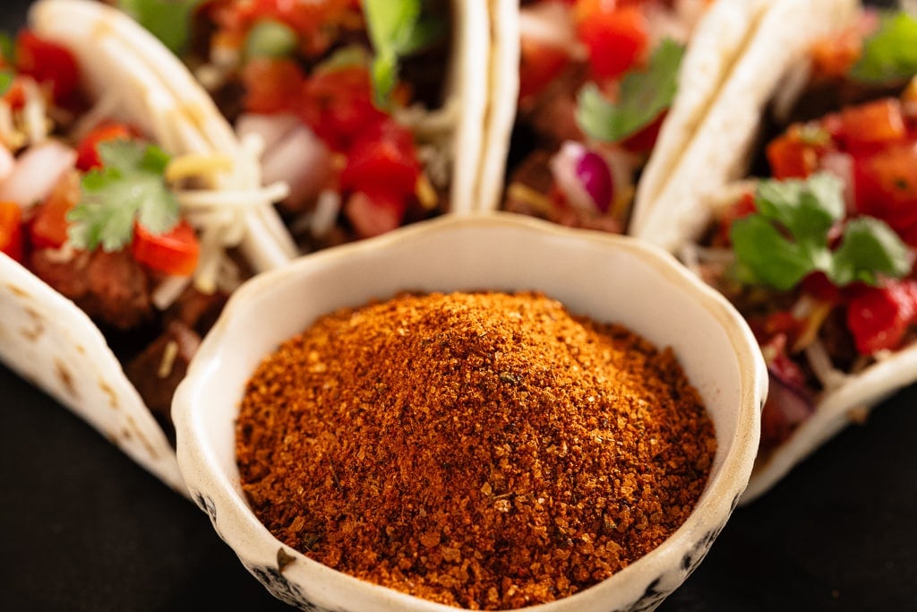 Bowl of fiesta rub in front of a row of carne asada tacos.