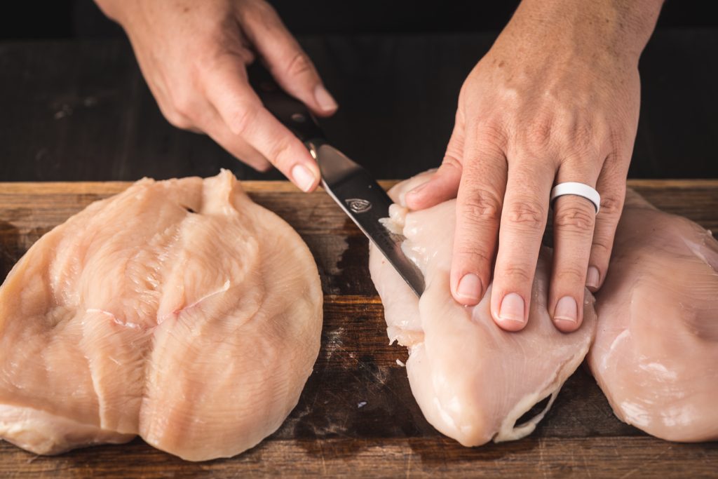 Chicken breasts being fileted open on a cutting board.
