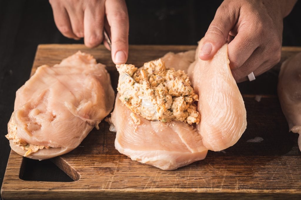 Cheese filling being stuffed in a chicken breast.