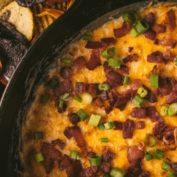 Smoked queso in a cast iron skillet topped with bacon and green onions.