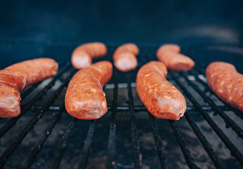 Italian sausage links liked up on the grill grates of a smoker.