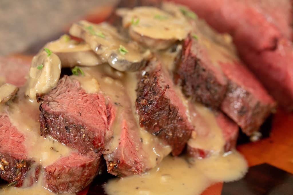 close up of sliced beef tenderloin topped with white wine mushroom gravy.