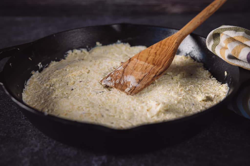 Cheese mixture in a cast iron skillet with a wooden spatula.