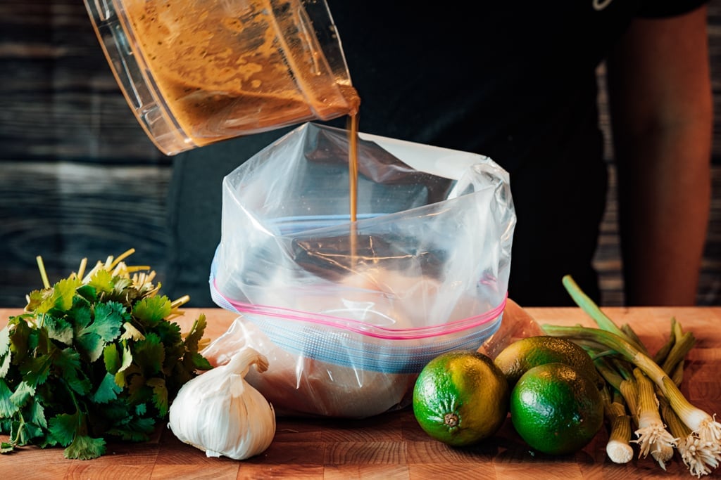Chili lime chicken marinade being poured into a zip top plastic bag surrounded by whole limes and garlic.