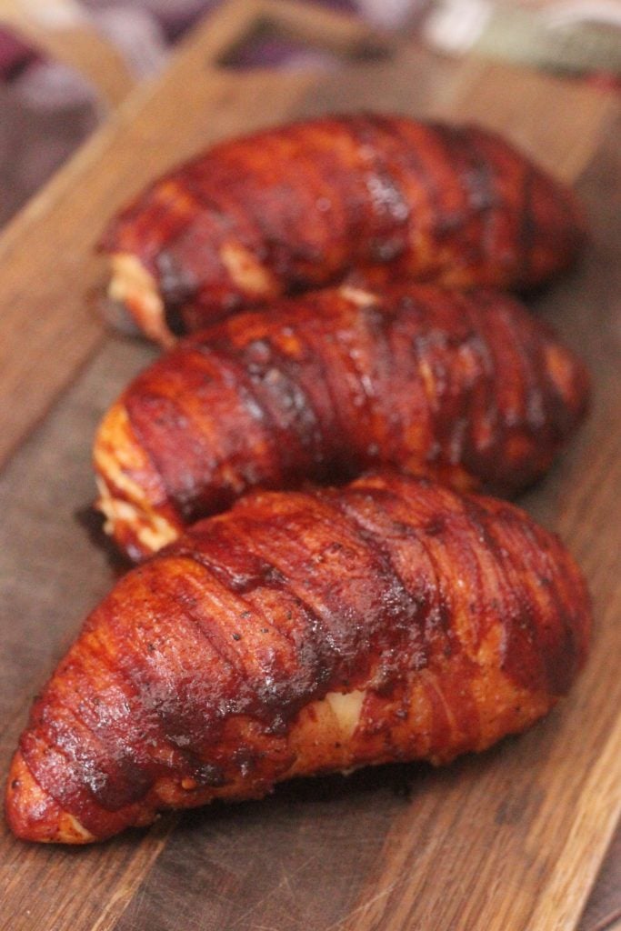 three bacon Wrapped Jalapeno Popper Stuffed Chicken breasts on a wooden cutting board