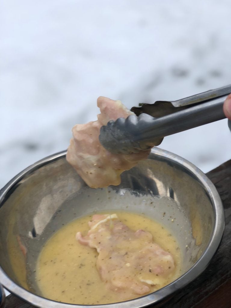 Frozen, raw chicken thigh being dunked in a dressing.