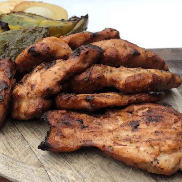 smoky grilled chicken thighs on a wooden serving platter next to grilled vegetables