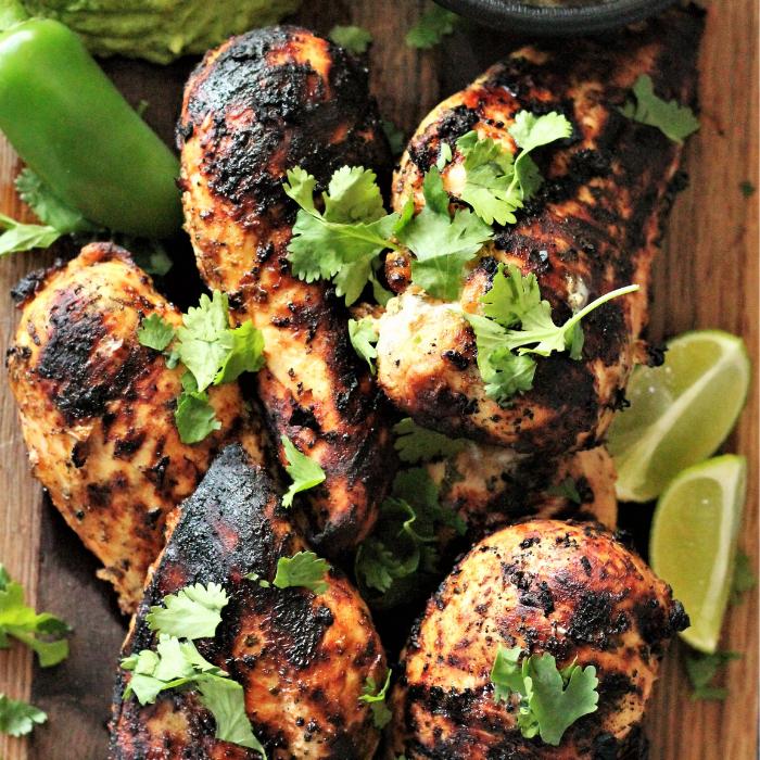 grilled chili lime chicken on a wooden cutting board topped with fresh cilantro and lime wedges