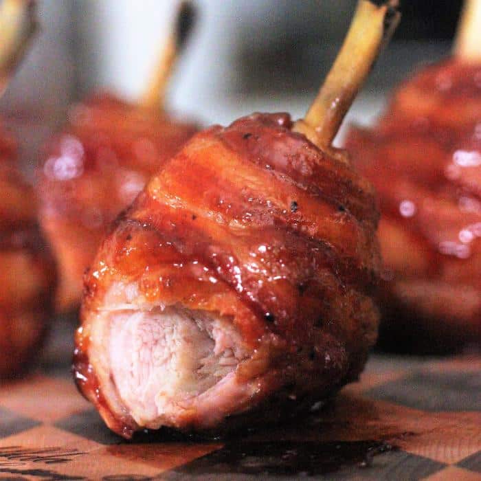 bacon wrapped chicken lollipop with a bite taken out on a wooden cutting board