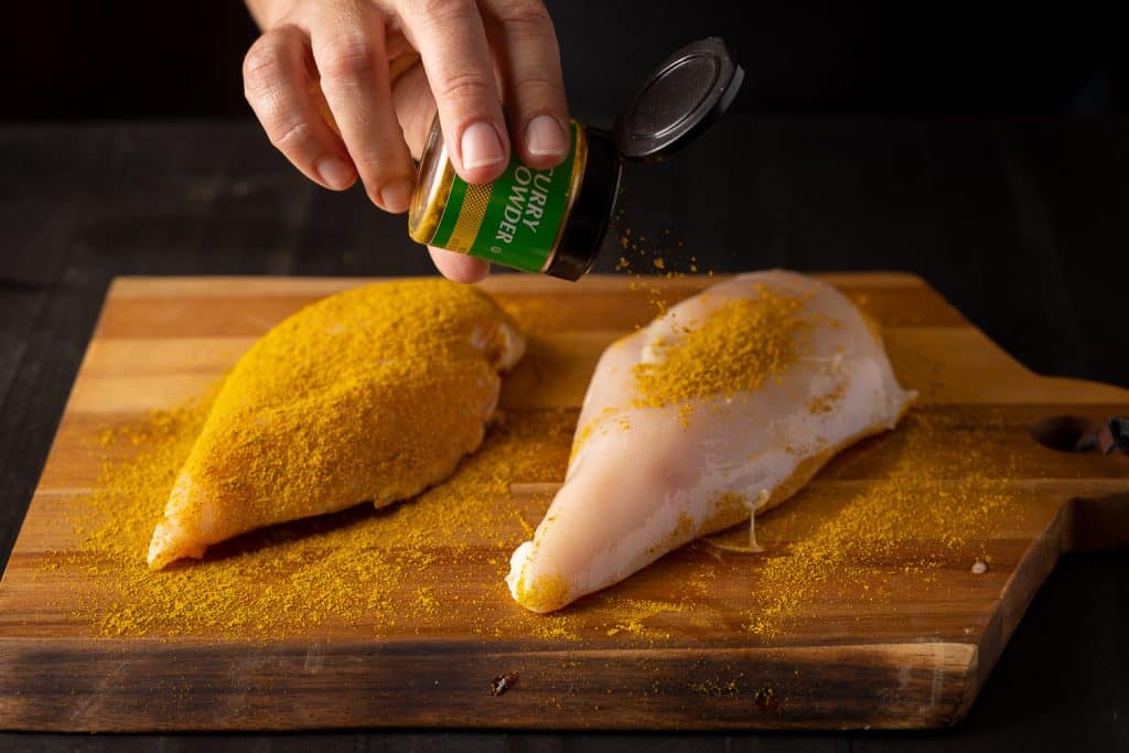 Chicken breasts being seasoned with curry powder.