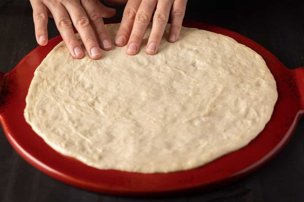 Pizza dough being formed on a pizza stone.