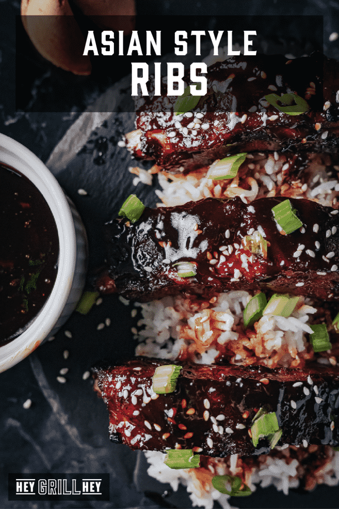 Smoked Asian style ribs garnished with sesame seeds over a bed of rice with text overlay - Asian Style Ribs.