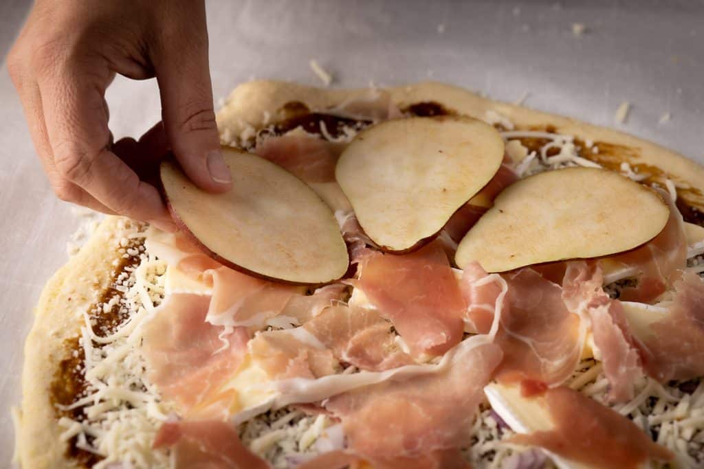 Pear slices being added to a deep dish pizza.