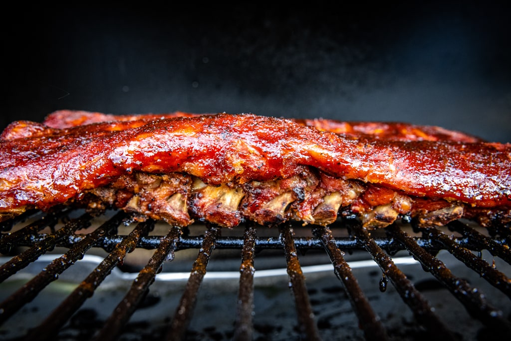 Braised and sauced Dr. Pepper ribs on the grill grates of a smoker.