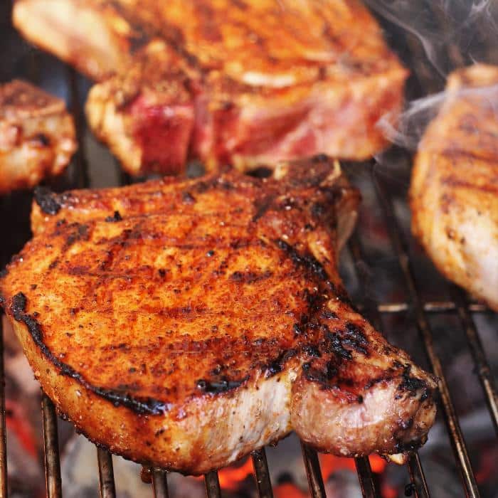grilled pork chops on a grill grate over hot coals. 