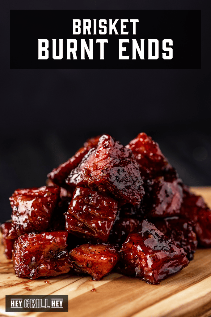 Stack of burnt ends on a wooden cutting board with text overlay - Brisket Burnt Ends.