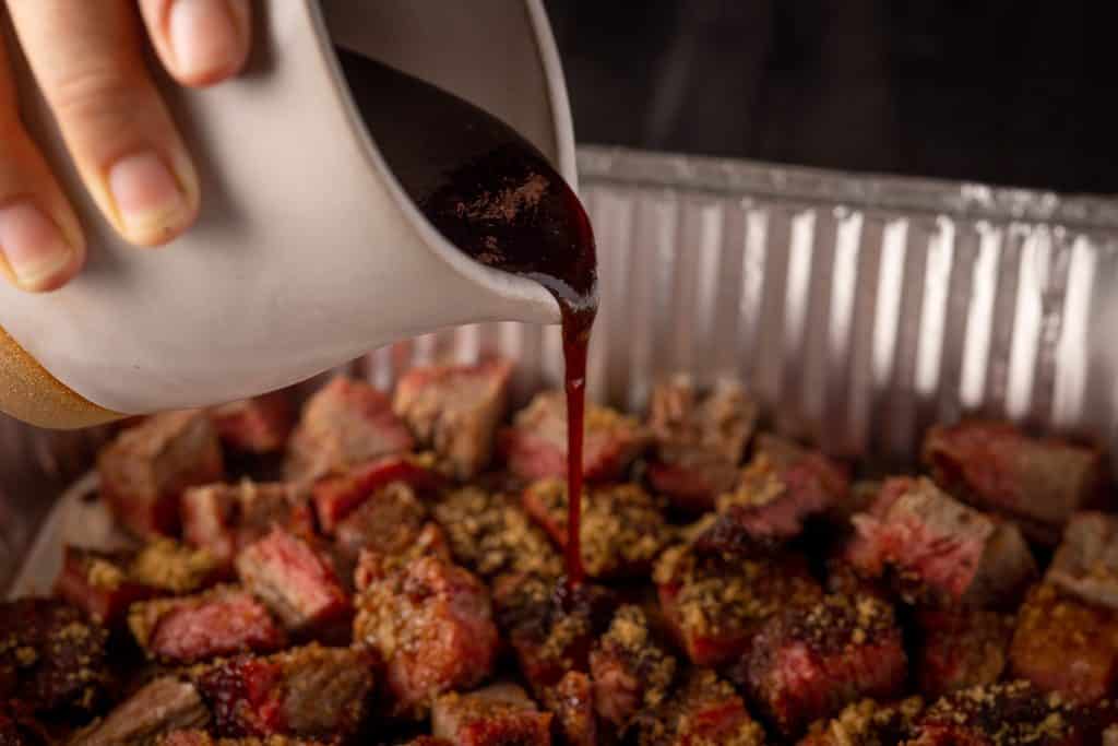 Burnt ends being covered with BBQ sauce and brown sugar.