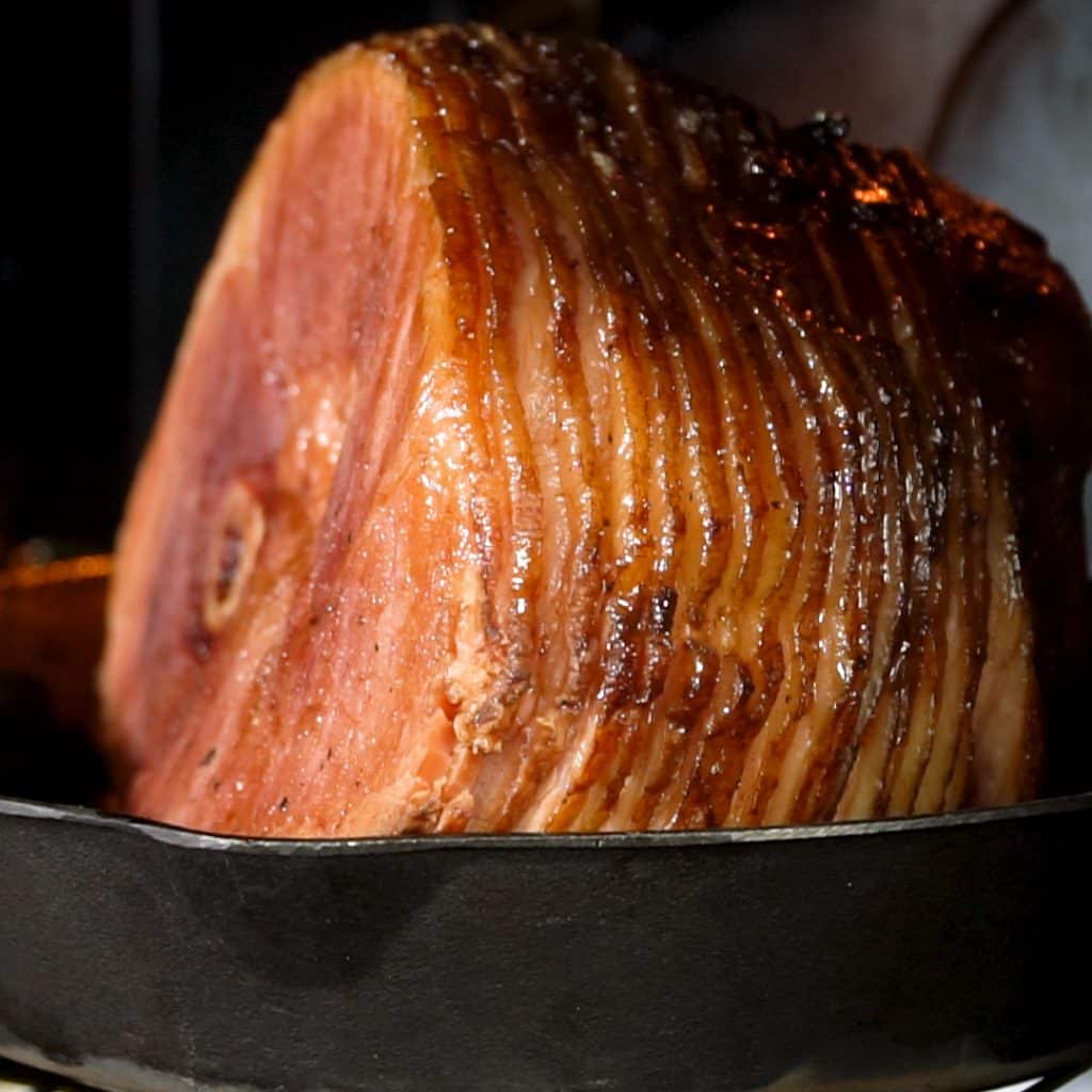 Twice smoked spiral ham with a glaze on top, sitting in a cast iron skillet.