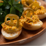 Smoked deviled eggs each topped with a pickled jalapeno arranged on a wooden serving plate.