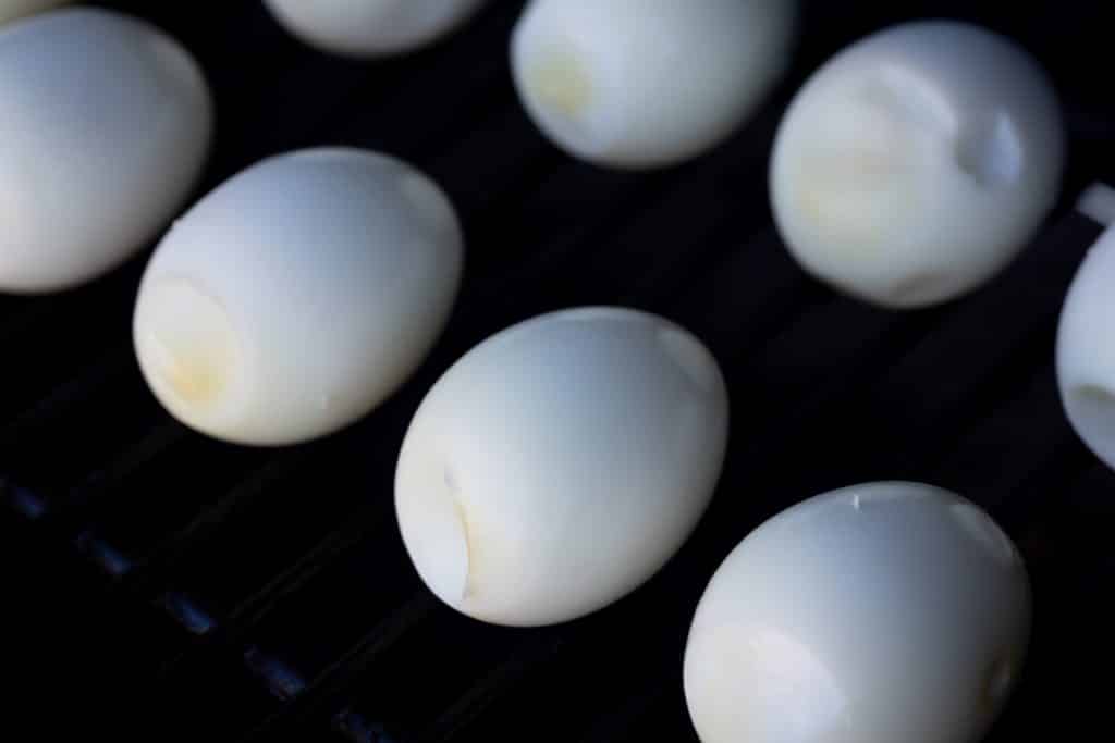 Peeled eggs on the grill grates of a smoker.