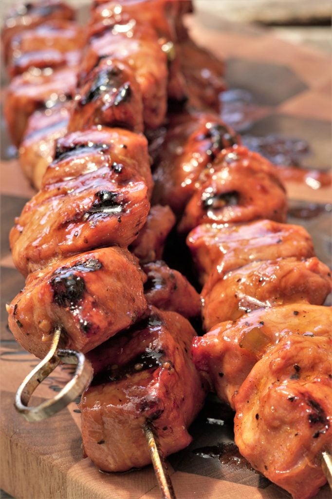 Small cubes of grilled pork on kebabs and resting on a wooden cutting board.