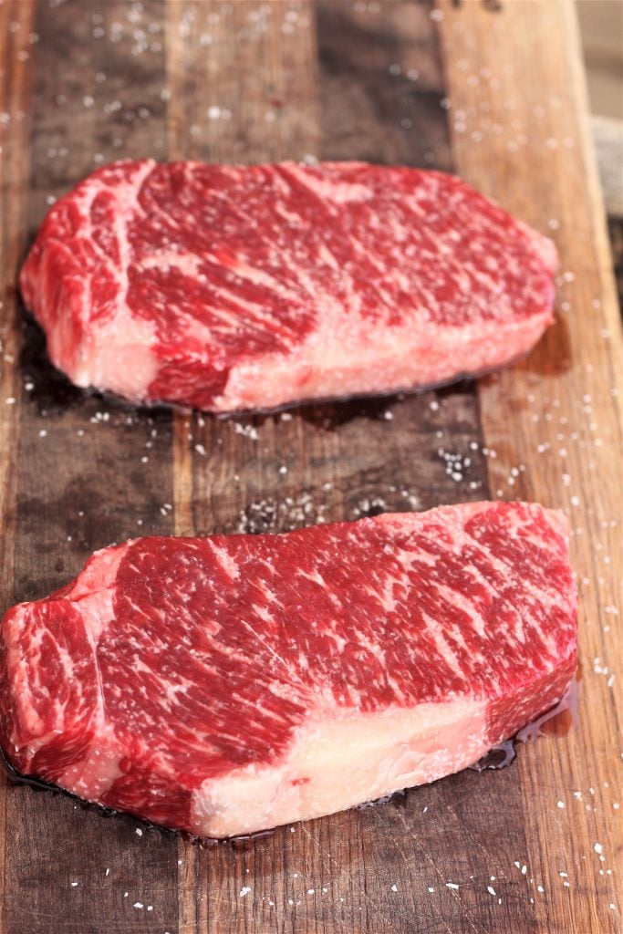 two ny strip steaks on a wooden cutting board