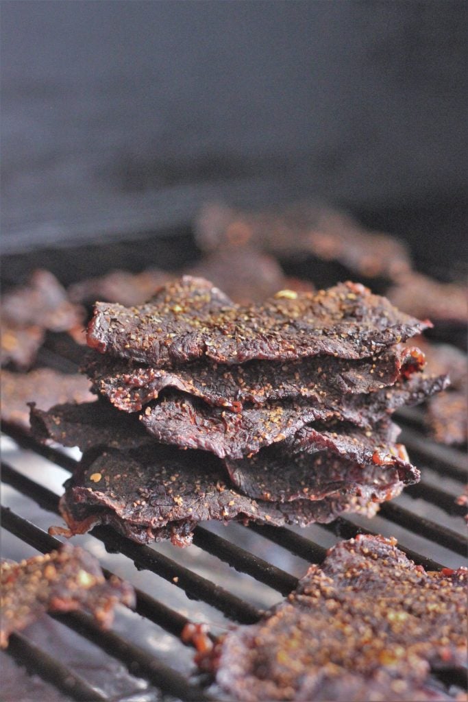 slices of beef jerky on the grill grates of a smoker.