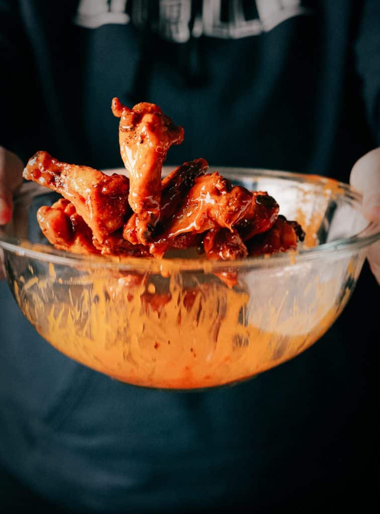 Chicken wings being tossed in Buffalo sauce.
