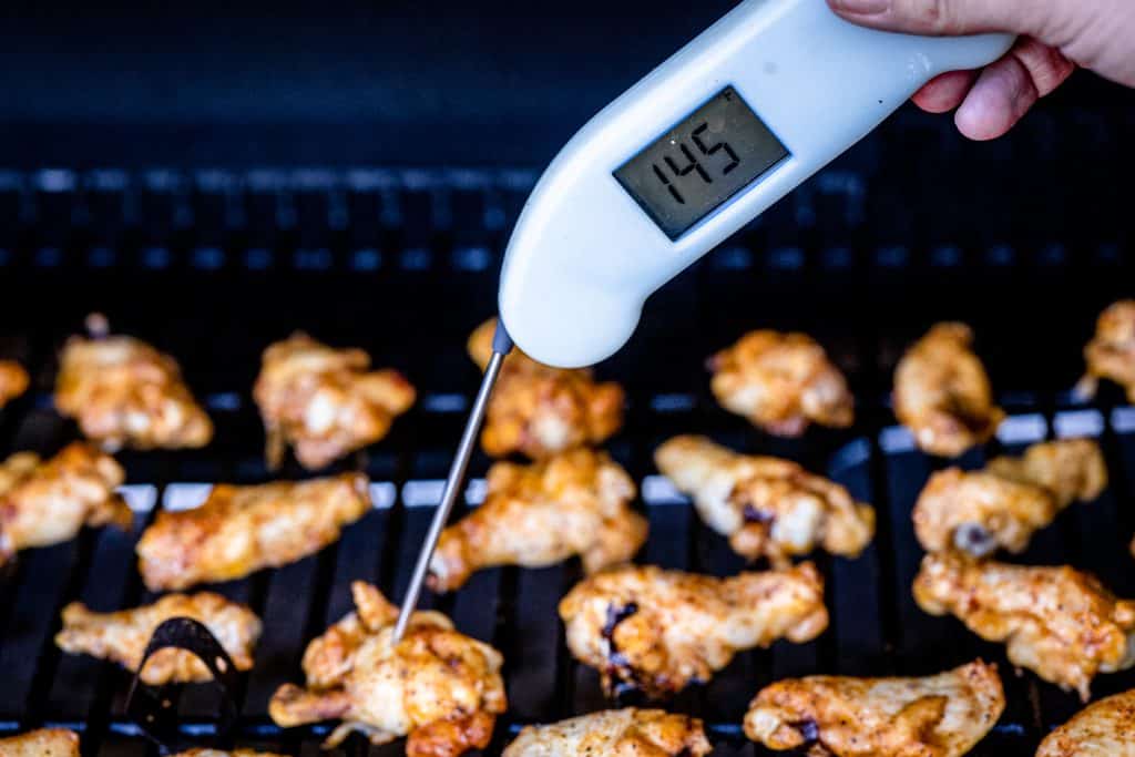 Chicken wings on the smoker with a thermometer reading a chicken wing at 145 degrees F.