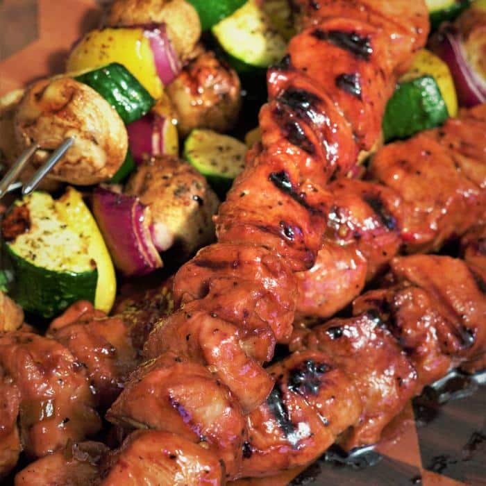asian bbq pork kabobs next to vegetable kabobs on a wooden cutting board