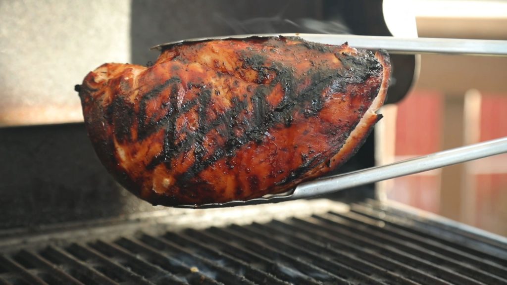 Smoked turkey breast being held above grill grates with a pair of tongs.