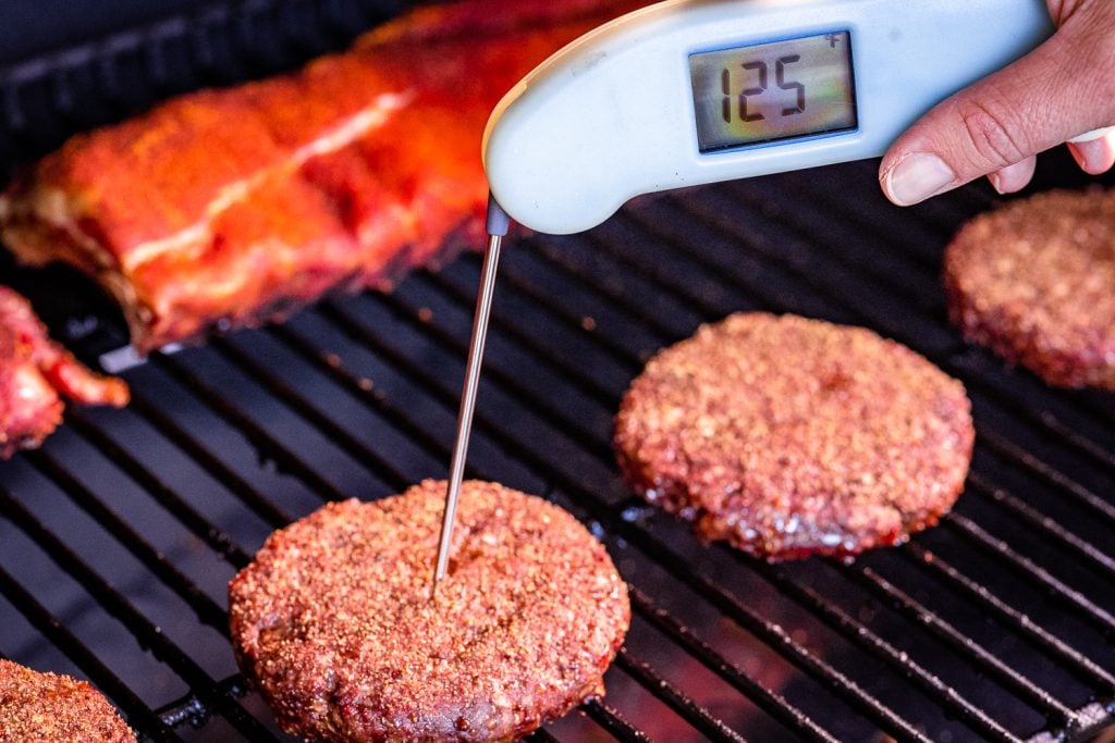 Hamburger patties on the grill reading a temperature of 125 degrees F.