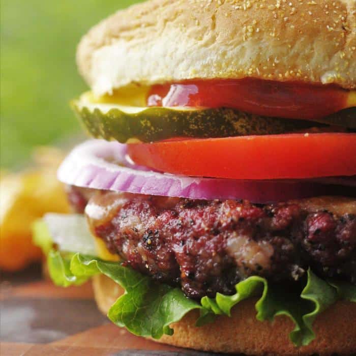 Smoked hamburger topped with pickle, tomato, onion, and lettuce on sesame seed bun.