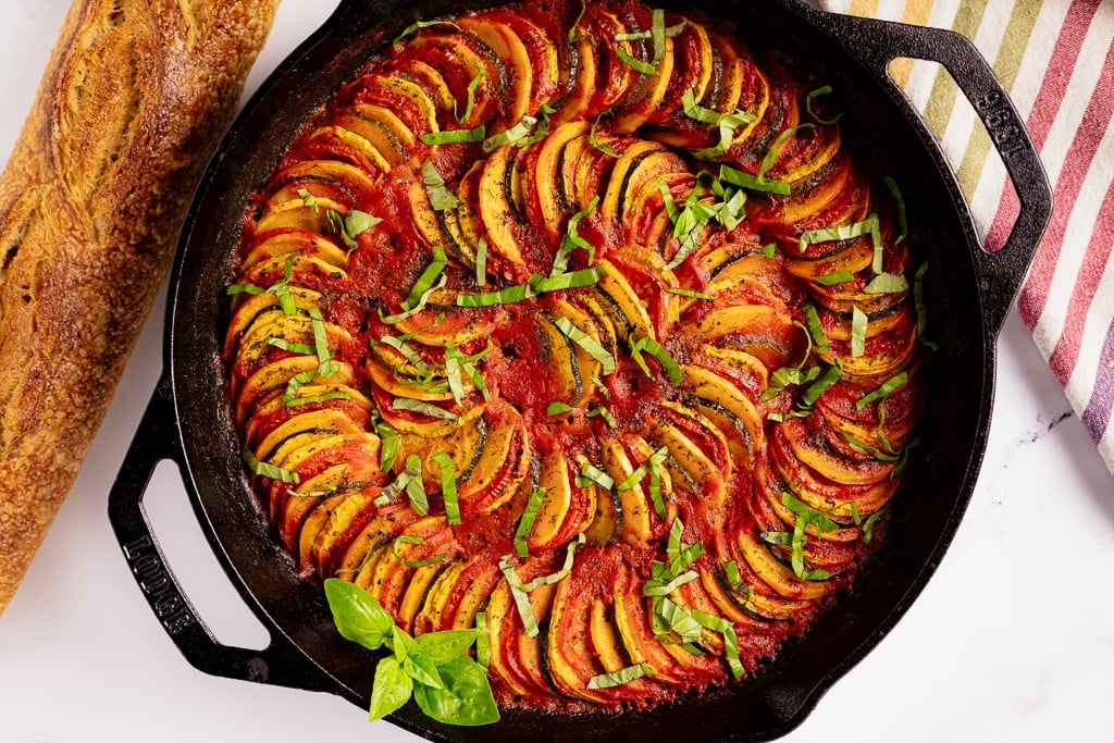 Grilled ratatouille in a cast iron skillet next to a baguette of bread.