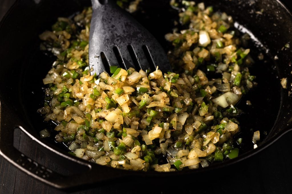 Chopped onions and green bell peppers in a cast iron skillet.