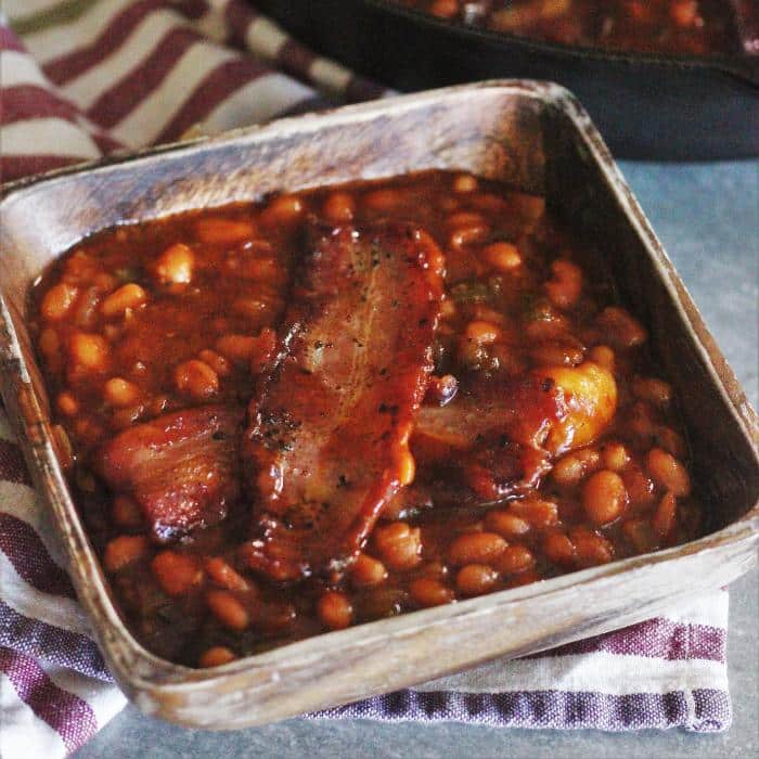 Smoked baked beans in a wooden bowl on top of a striped kitchen towel.