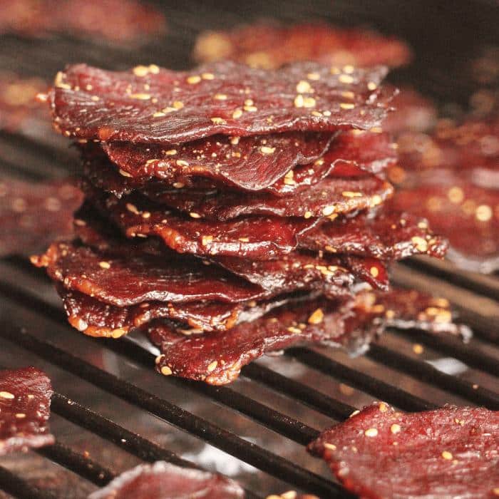 Stack of teriyaki beef jerky on the grill grates of a smoker.