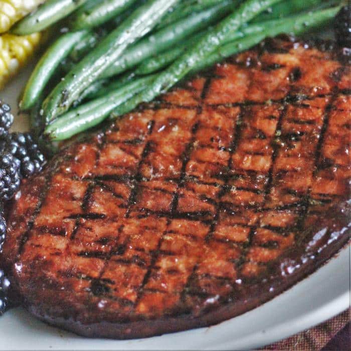 grilled ham steak on a white plate next to blackberries and string beans