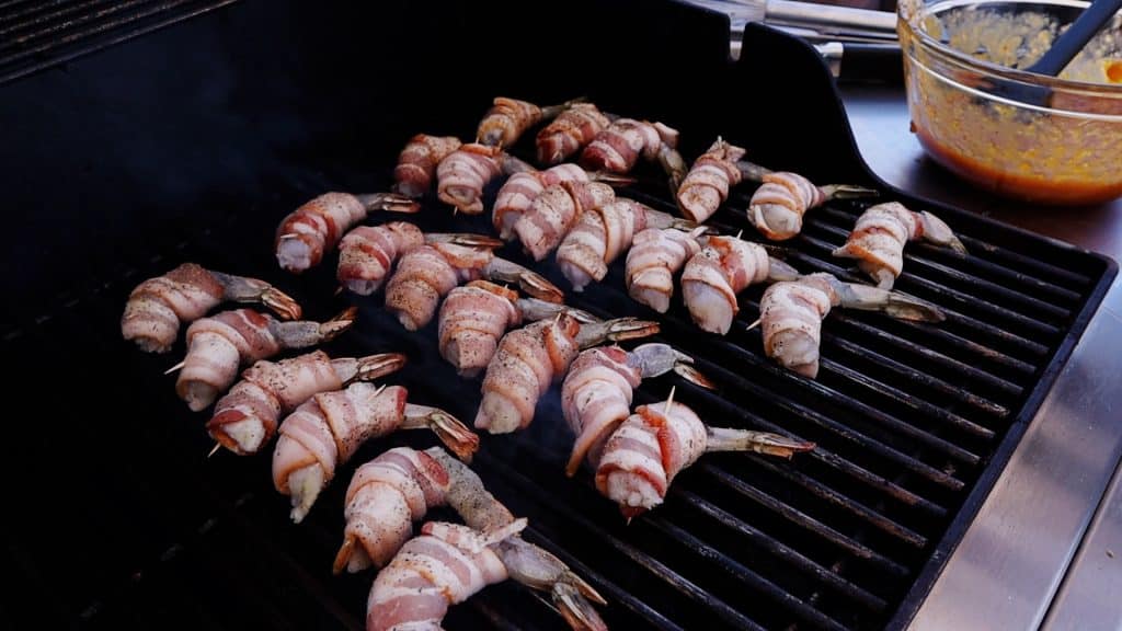Bacon wrapped shrimp lined up on a grill.