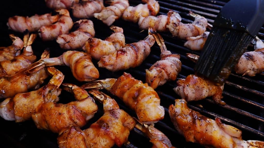 Bacon wrapped shrimp on a grill being glazed.