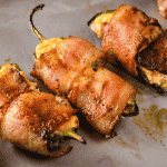 Three grilled jalapeno poppers on a serving dish.