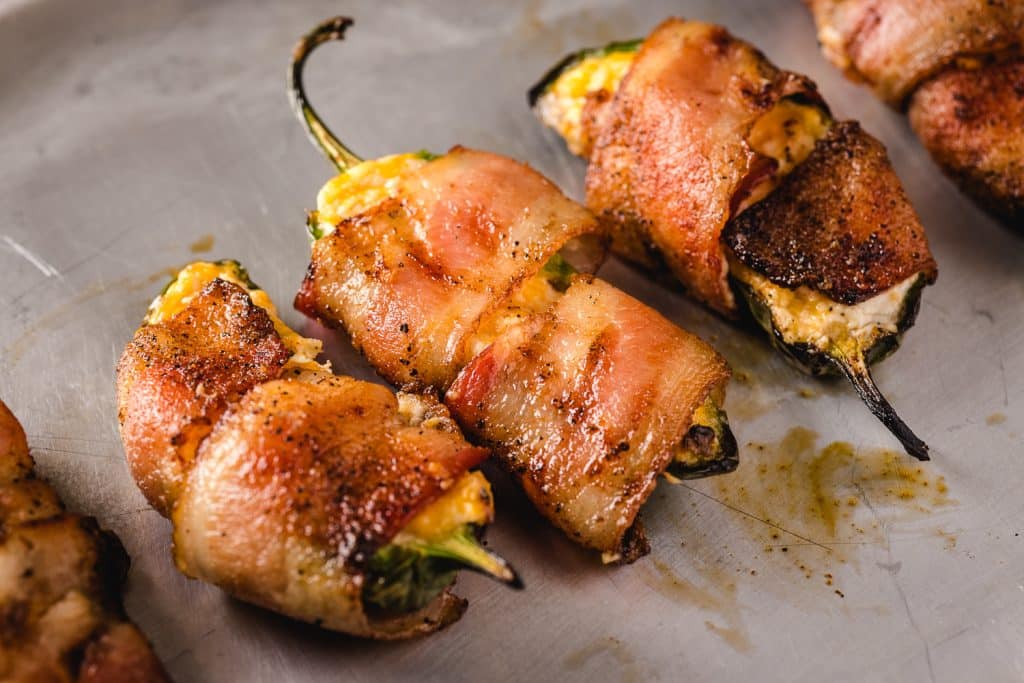 Three grilled jalapeno poppers on a serving dish.