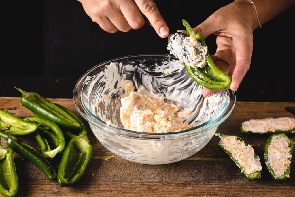 Cream cheese filling being spooned into a jalapeno half.