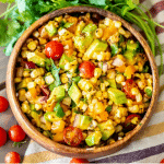 A wooden bowl of grilled corn salad over a striped dish towel.