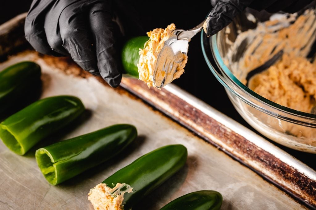 Jalapenos being stuffed with a cream cheese filling.