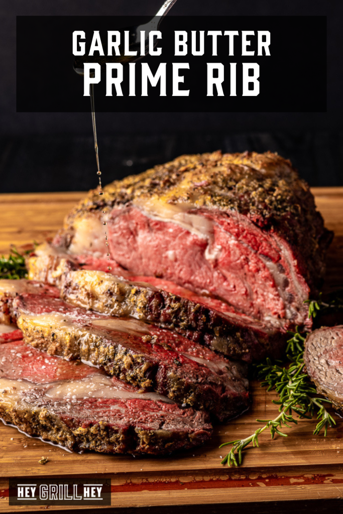Sliced prime rib on a wooden cutting board being drizzled with garlic butter with text overlay - Garlic Butter Prime Rib.