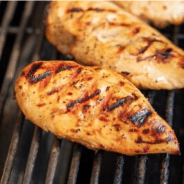 Two marinated whole grilled chicken breasts on the grill grates of a gas grill.