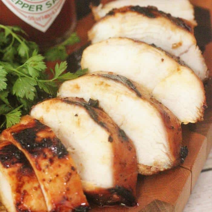 sliced sweet heat marinated grilled chicken breast on a wooden cutting board next to fresh herbs