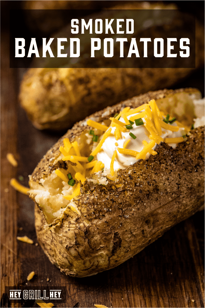 Smoked baked potato topped with shredded cheese and sour cream with text overlay - Smoked Baked Potatoes.