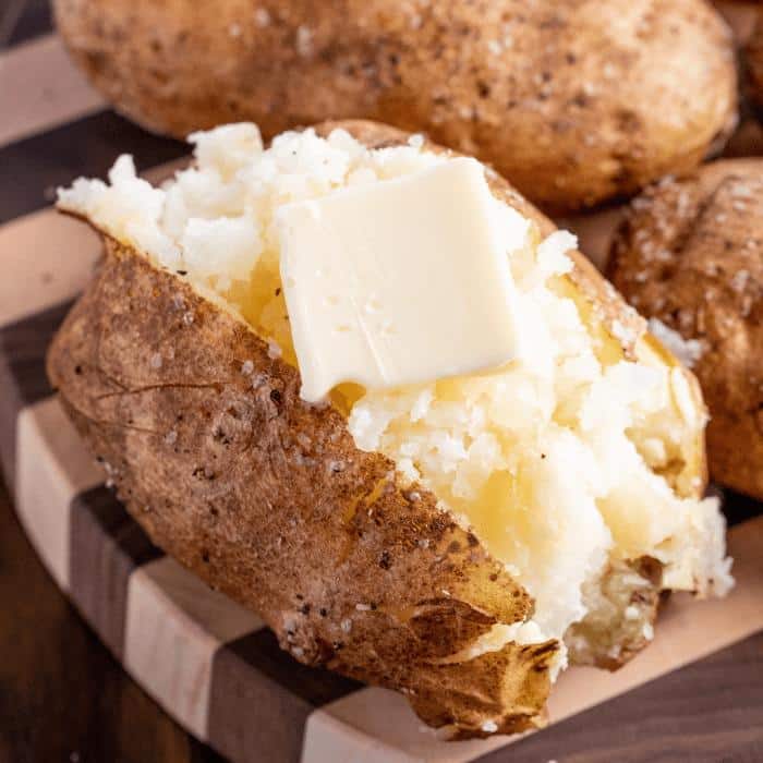 Sliced and fluffed smoked baked potato garnished with a pad of butter, salt, and pepper.